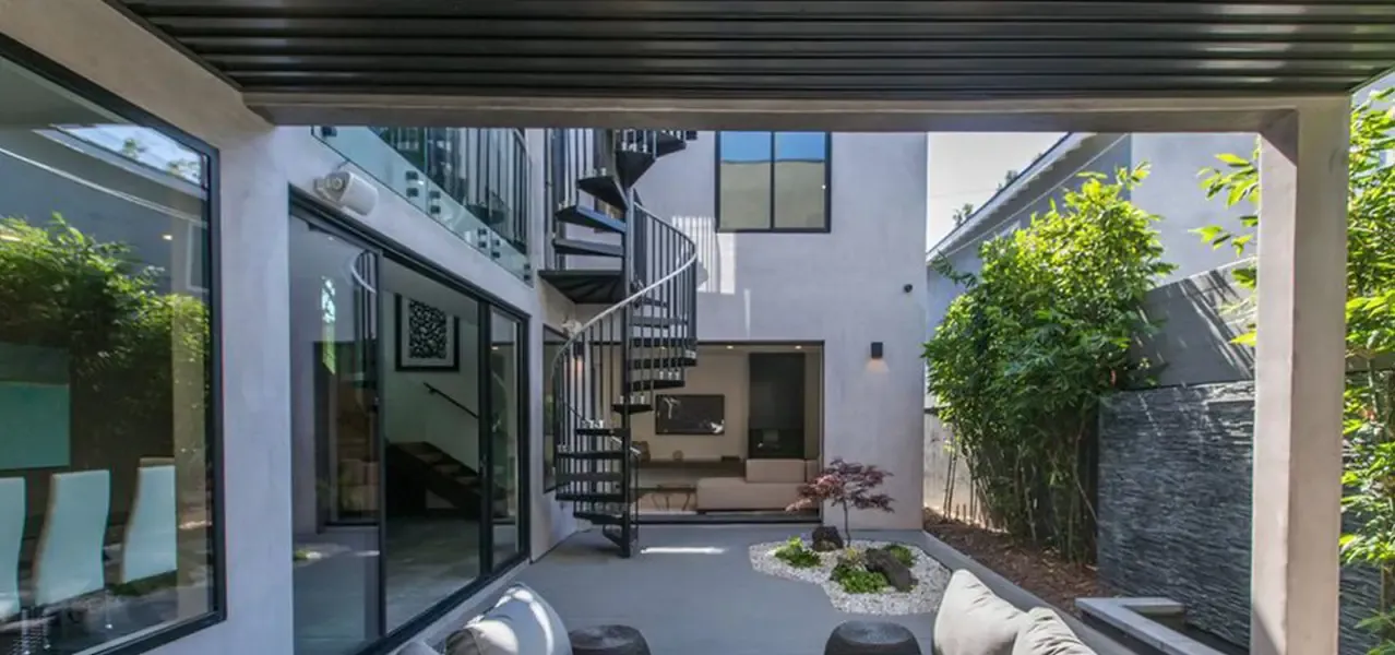 Modern minimalist courtyard with sleek black spiral staircase connecting two levels, contemporary outdoor seating, and Japanese maple tree in white gravel garden.