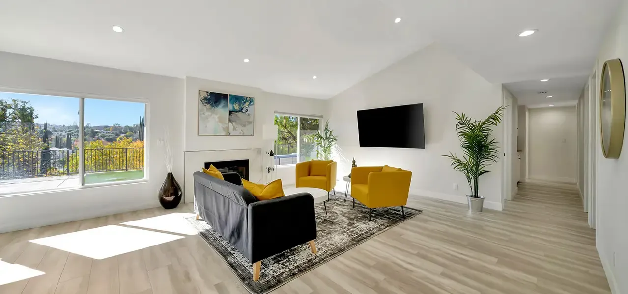 A modern living room with black sofa, yellow armchairs, light wood flooring, and sliding glass door to outdoor space