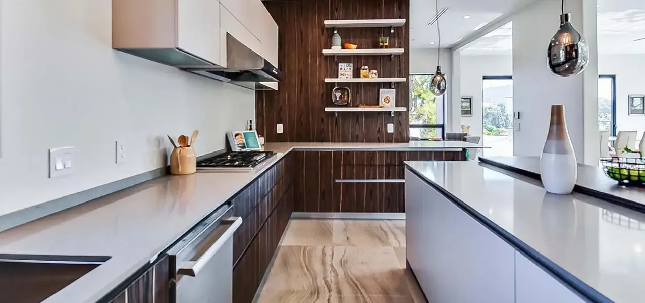A modern, open-concept kitchen with sleek, dark wood cabinetry, light gray countertops, and stainless steel appliances including a gas cooktop and range hood.